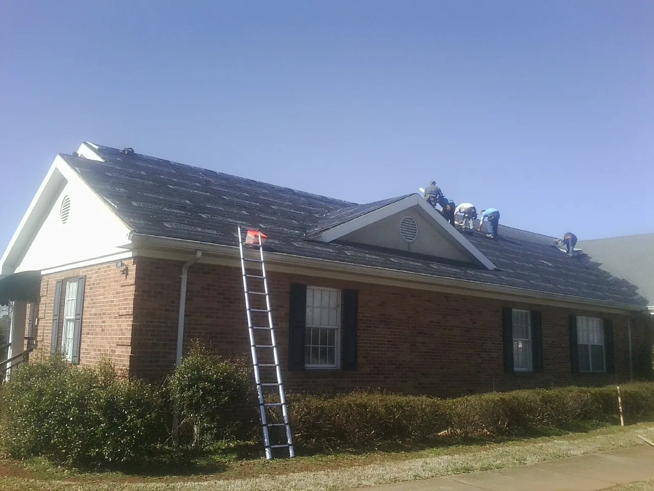 Crew tearing shingles off a brick ranch roof with a ladder set — Metal Roof Repair work by our crew in Running Springs
