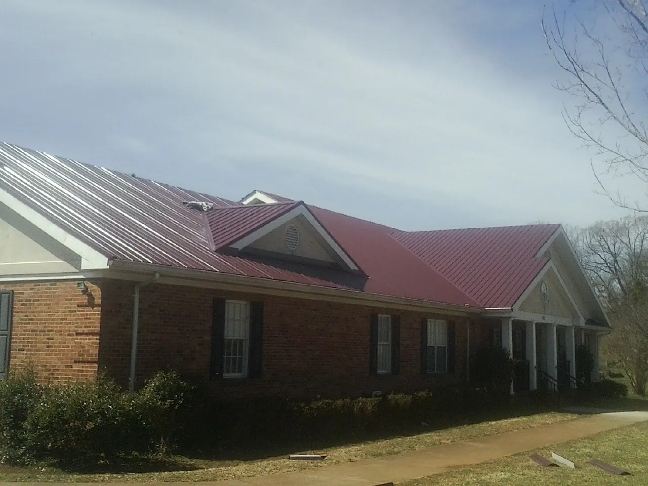 Red metal roof with gabled entries on a long brick building, from a Hail Damage Roof Repair job in Running Springs