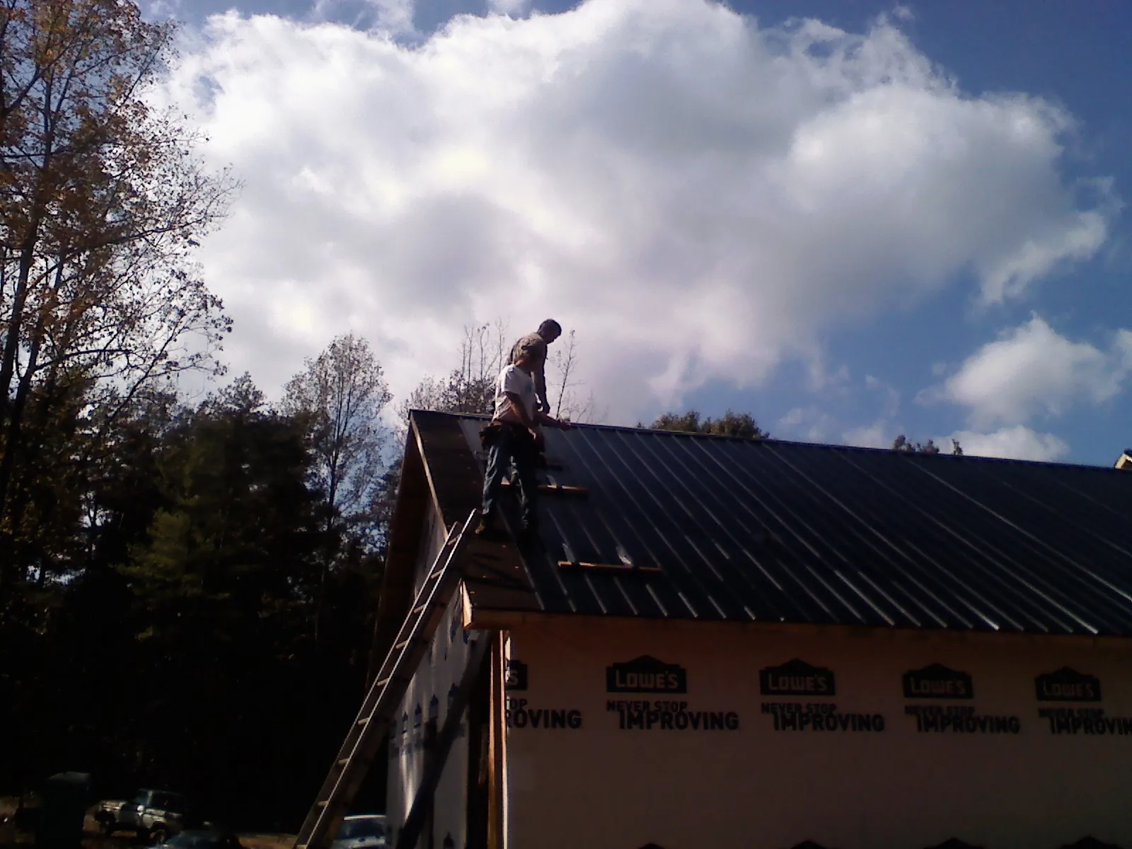 Roofer fastening dark metal panels high against a cloudy sky, from a Roof Inspection job in Running Springs
