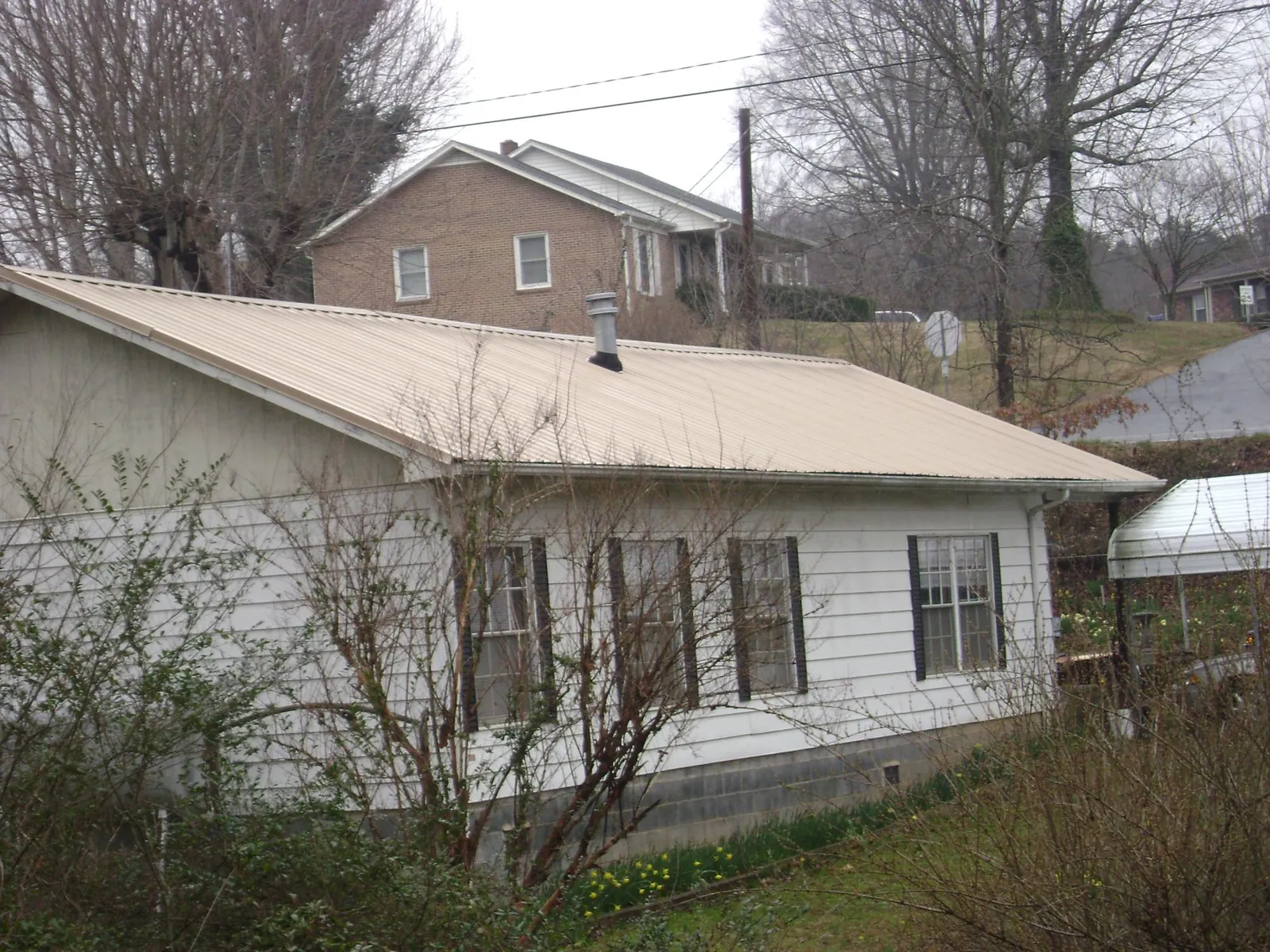 Tan metal roof on a white sided house set into a hillside — Commercial Roofing by Roofing Brothers in Running Springs